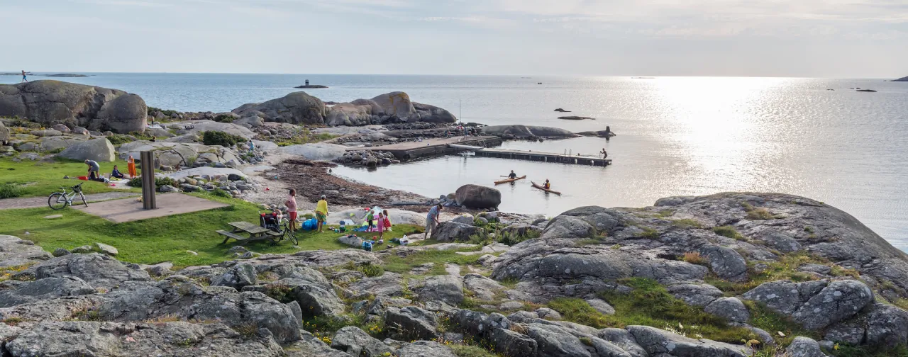 En naturskön badplats i Göteborgs skärgård där familjer solar, badar och paddlar kajak en varm sommardag.