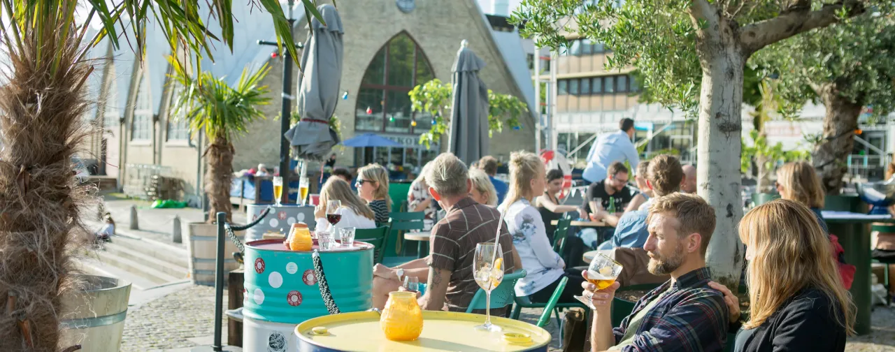 Avkopplande uteservering vid Feskekôrka i Göteborg en solig dag, med människor som njuter av mat och dryck.