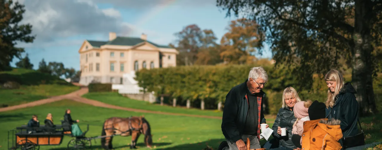 Gunnebo Slott erbjuder en idyllisk miljö för picknick och utflykter. Här syns en familj njuta av en solig dag med häst och vagn i bakgrunden.