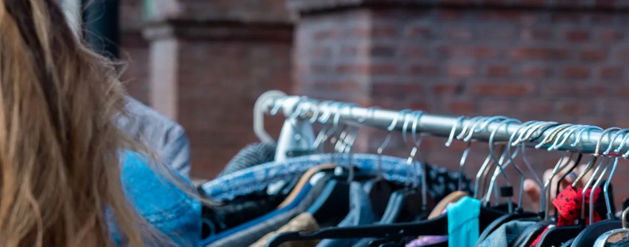 En person bläddrar genom kläder på en second-hand-marknad i Göteborgs Linnéområde, känt för sina vintagebutiker och unika affärer.