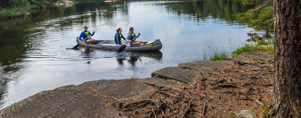 Tre personer paddlar kanot på en stilla sjö omgivet av grönskande skog. Populär utflykt i Göteborgs natur.