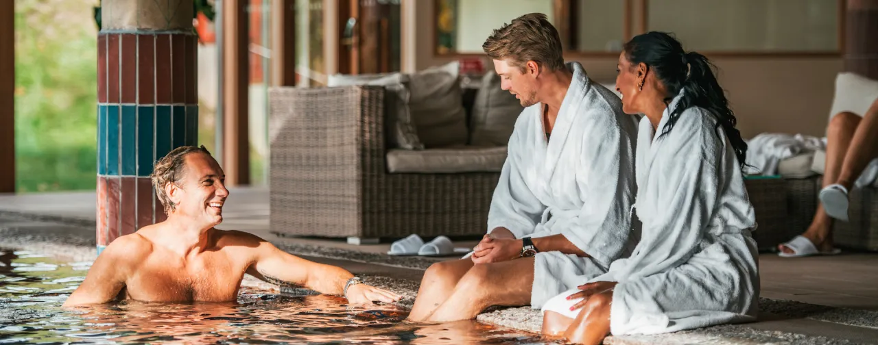 Tre personer i vita badrockar kopplar av vid en inomhuspool på ett av Göteborgs spahotell. Staden erbjuder flera spa- och wellnessupplevelser, från lyxiga hotellspa till bastubad vid havet – perfekt för återhämtning och avkoppling.