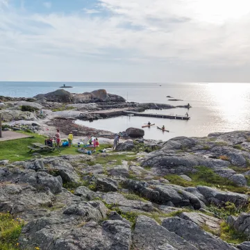 En naturskön badplats i Göteborgs skärgård där familjer solar, badar och paddlar kajak en varm sommardag.