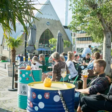 Avkopplande uteservering vid Feskekôrka i Göteborg en solig dag, med människor som njuter av mat och dryck.