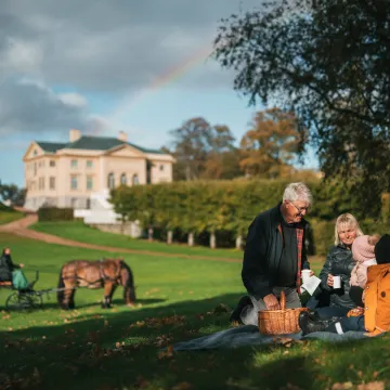 Gunnebo Slott erbjuder en idyllisk miljö för picknick och utflykter. Här syns en familj njuta av en solig dag med häst och vagn i bakgrunden.