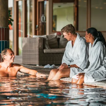 Tre personer i vita badrockar kopplar av vid en inomhuspool på ett av Göteborgs spahotell. Staden erbjuder flera spa- och wellnessupplevelser, från lyxiga hotellspa till bastubad vid havet – perfekt för återhämtning och avkoppling.